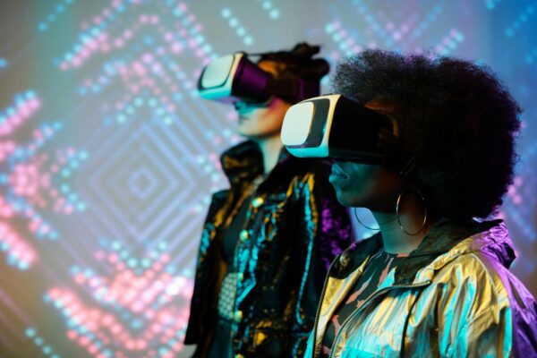 Two individuals wearing virtual reality (VR) headsets, immersed in a digital experience with colourful abstract lights in the background.